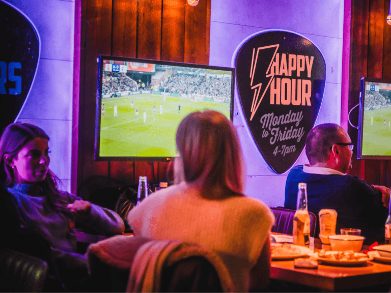 A group of people watching Premier League football on large screens in a Belushi's Bar.