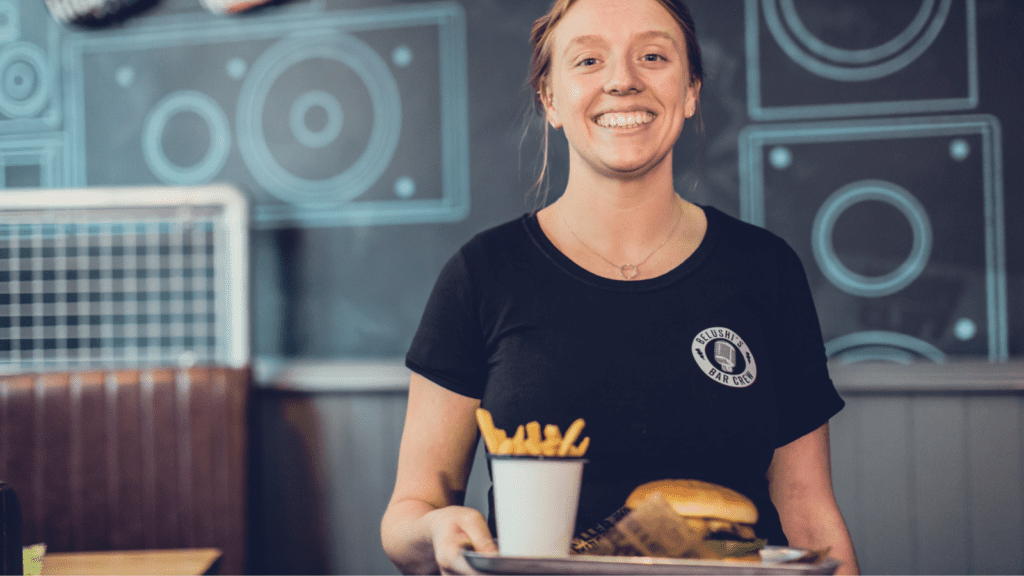 A female member of staff at Belushi's serves a burger and fries.