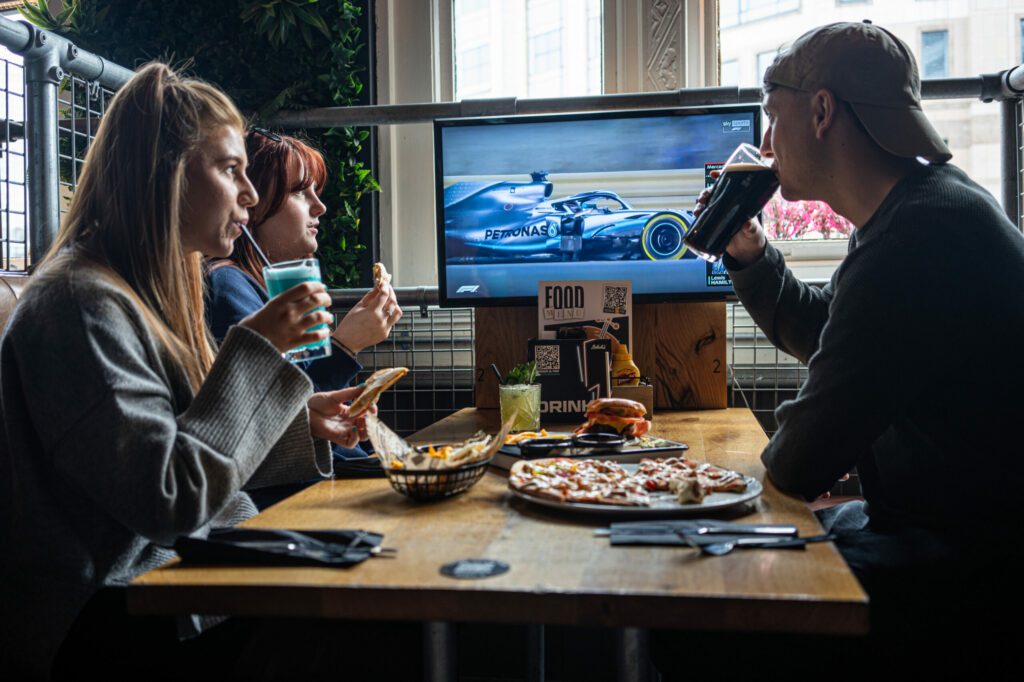 Friends enjoy a drink and some food whilst watching the F1 at a Belushi's Bar.