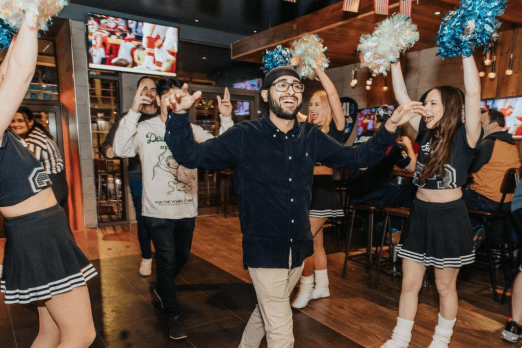 A man walks in to a Belushi's Bar with a cheerleader guard of honour.