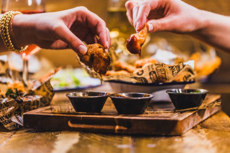 Friends dipping chicken wings into sauce at a Belushi's Bar.