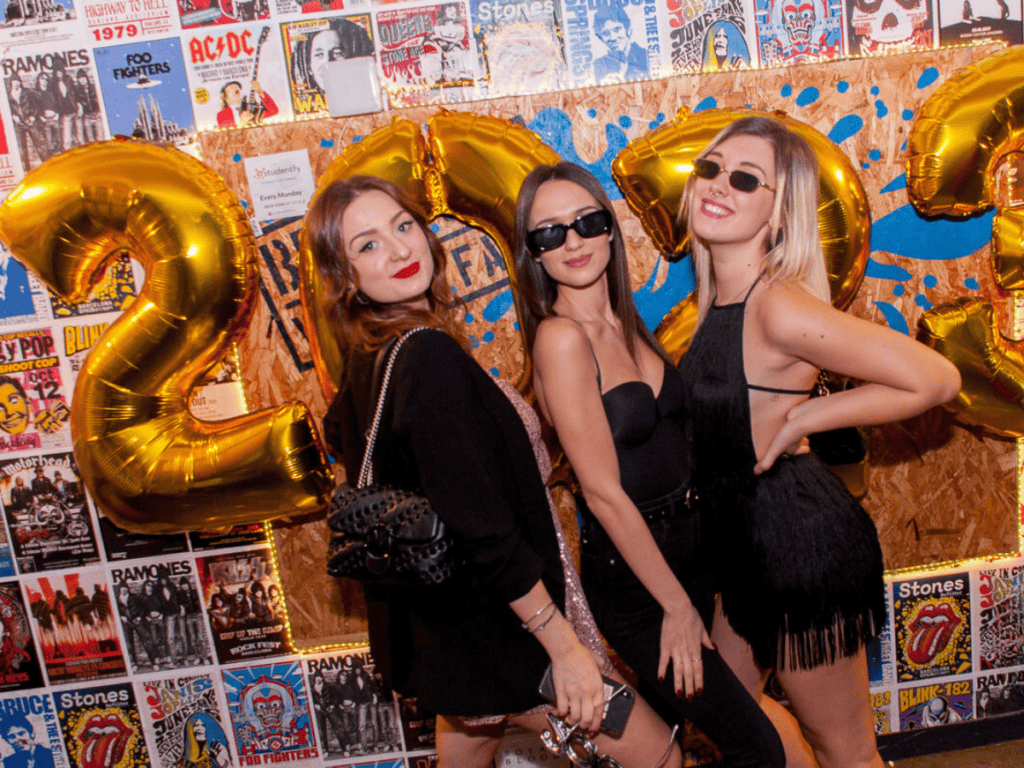 Three friends pose in front of balloons at a New Year's Eve party.