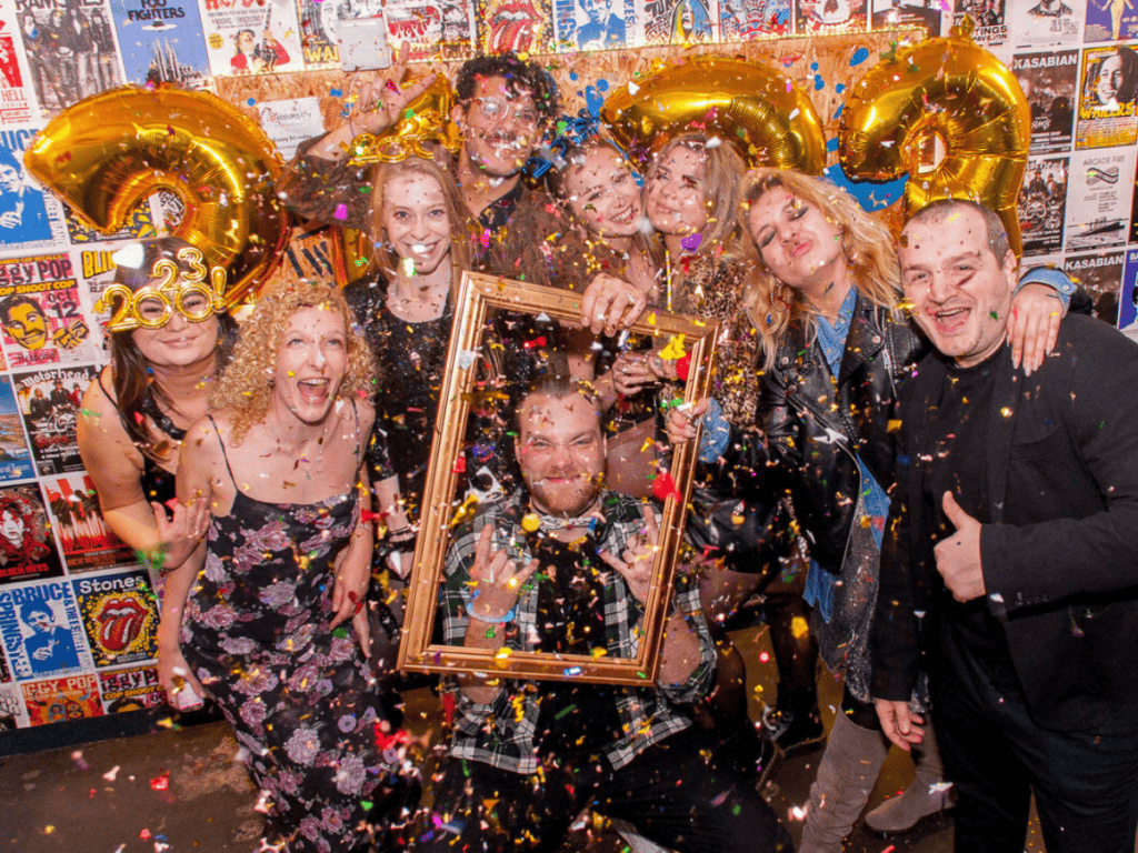 A group of friends surrounded by balloons and confetti at a Belushi's New Years Eve party.