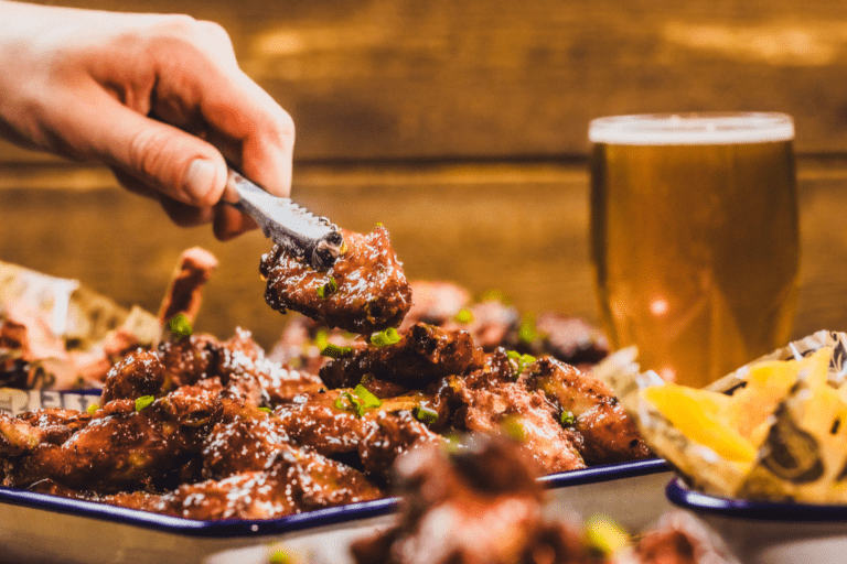 A chef serves a tasty-looking platter of chicken wings with a pair of tongs in a Belushi's Bar.