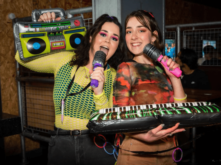 Two friends in 80's costumes sing karaoke in a Belushi's Bar.