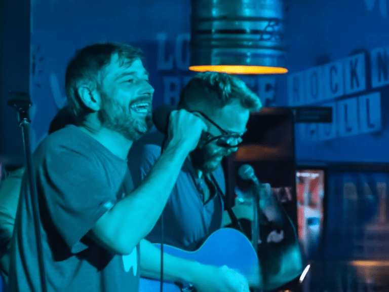 A band play music and sign under neon lights at a Belushi's Bar.