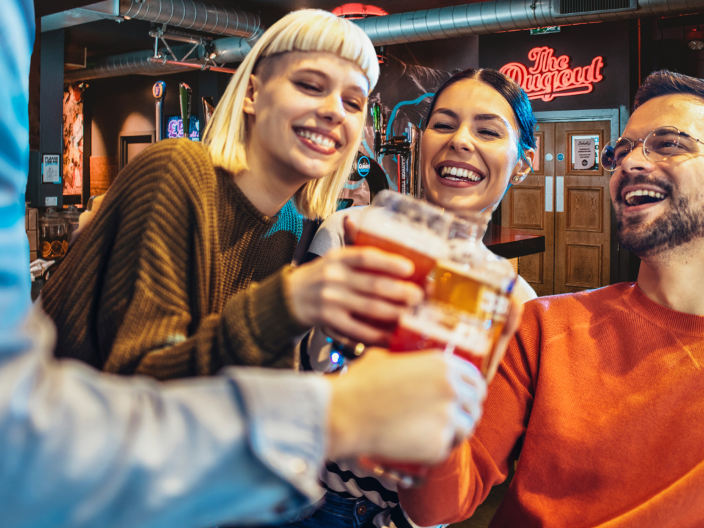 Friends laugh and cheers craft beers in a Belushi's Bar.