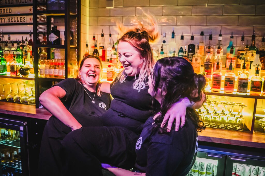 Friendly bartenders at a Belushi's Bar laugh and joke together.