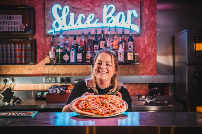 A pizza is served by a friendly bartender in a Belushi's Bar.