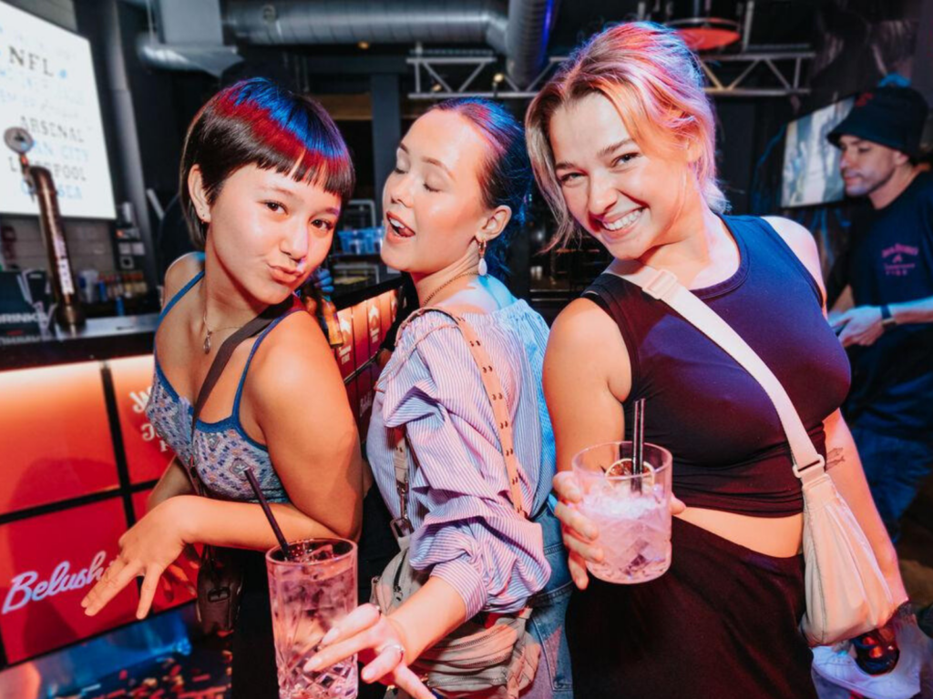 Three female friends dance and laugh in a Belushi's Bar.