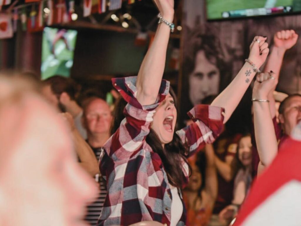 A young woman cheers in a bar while watching live sport