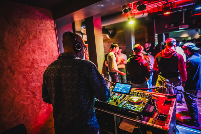 Picture of a DJ playing at a Belushi's bar, and customers dancing