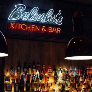 An image of the back bar of a Belushi's bar, with a neon sign that says Belushi's Kitchen & Bar