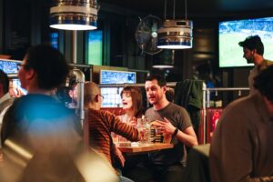 An image of a group of people sat at a booth, chatting and enjoying pints of beers, with HD screens all around them