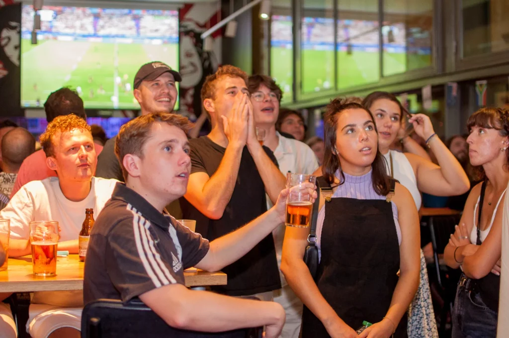 A group of customers at a Belushi's bar watching a game of football on large HD screens