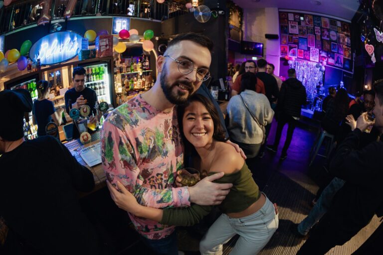 A couple of friends hug and smile for the camera while drinking at a Belushi's bar