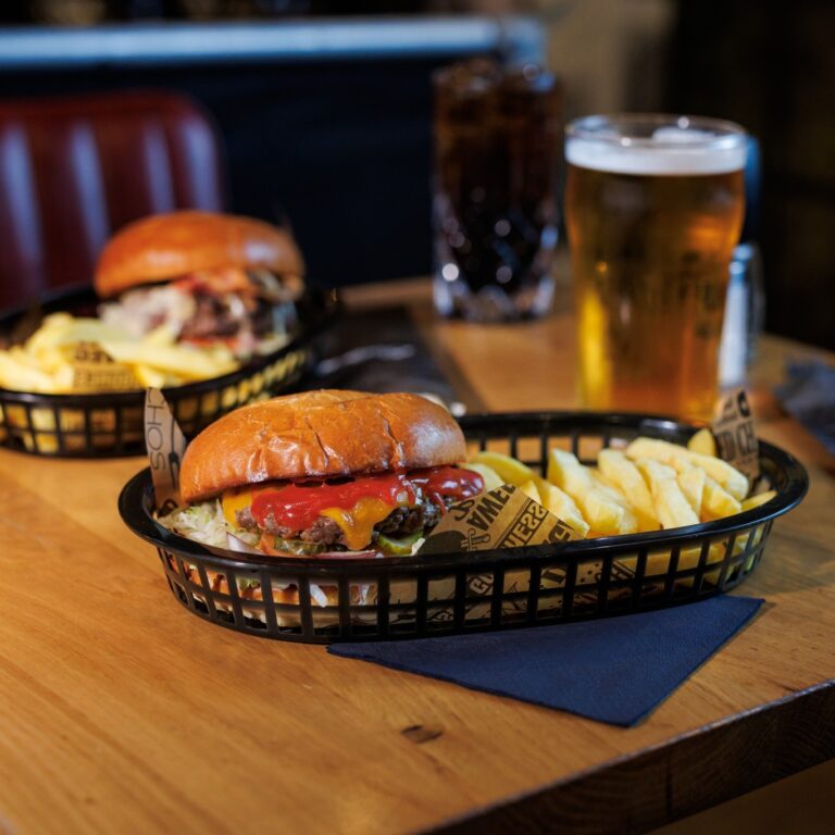 A basket set on a table with burger and fries, accompanied by a pint of beer.