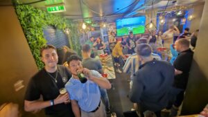 A picture of a group of customers playing beer pong at a Belushi's bar with football playing on HD screens