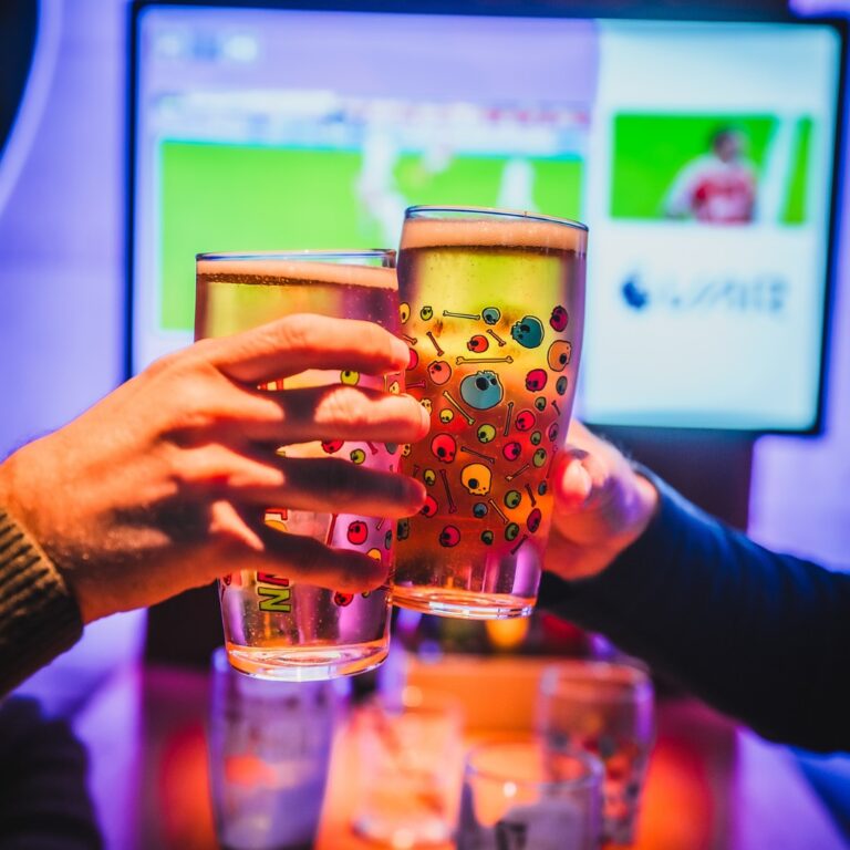 Two pints of beers cheersing in front of an HD screen showing football at a Belushi's bar