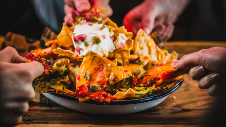 A plate of cheesy nachos being shared