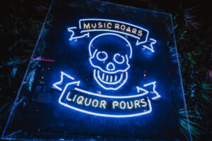 A picture of a neon sign with a skull, and writing that says 