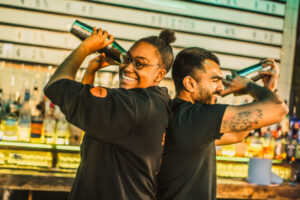 An image of two bartenders shaking cocktails, back to back