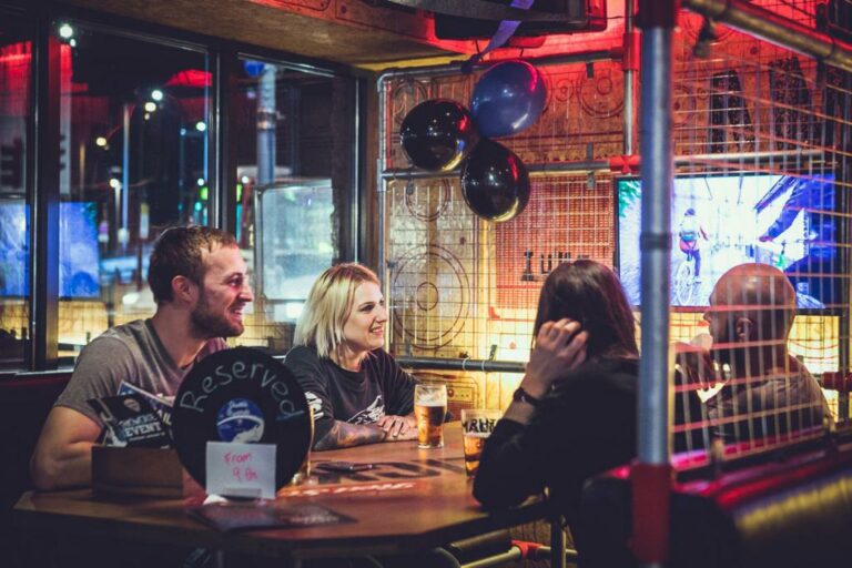 A picture of a group of friends sat in a caged booth, celebrating a birthday with pints of beers on the table