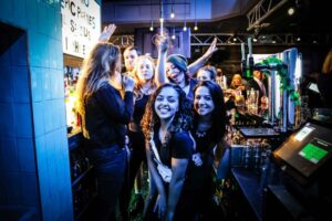 A group of bartenders pose and smile for the photo from behind the bar