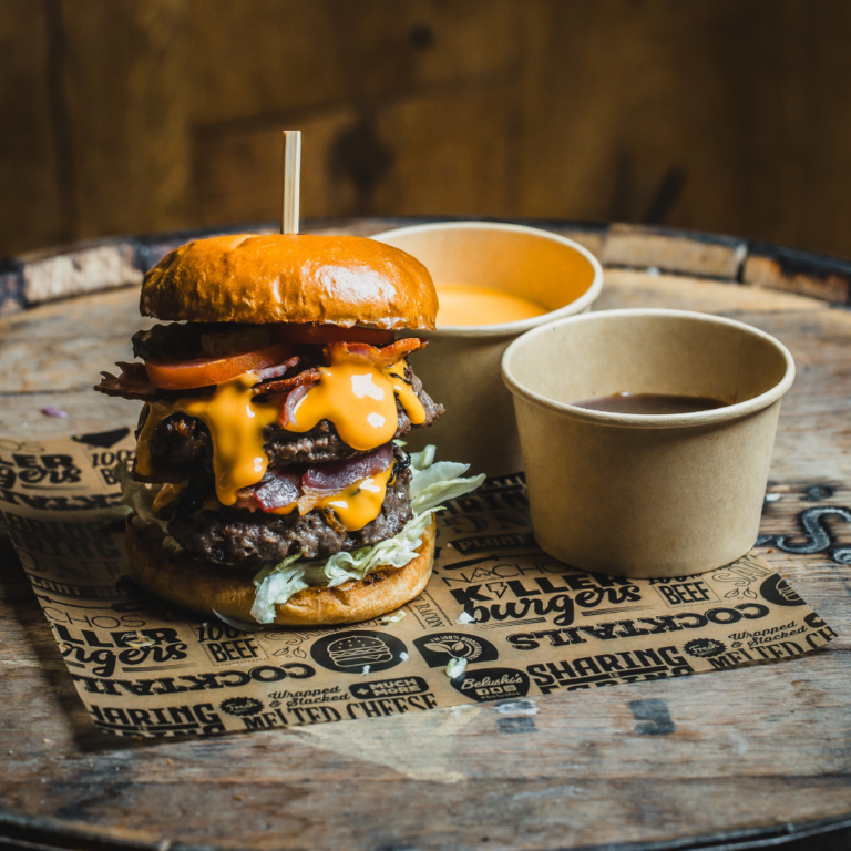 A double, large, cheesy burger with two ramekins of sauce on the side.