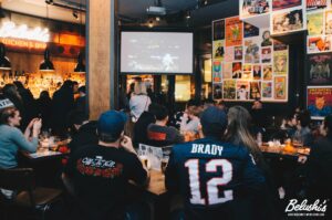 A picture of seated Belushi's customers watching a game on a large HD screen