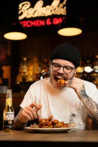 An image of a customer eating chicken wings and drinking a bottled beer