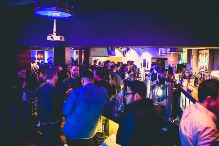 An indoor picture of Belushi's bar with customers standing and drinking