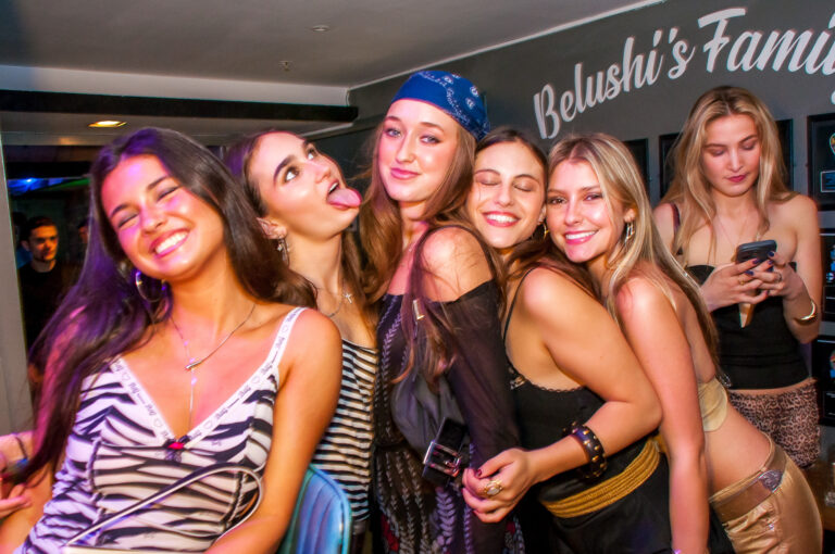 Group of young women posing closely for a photo at a party, smiling and having fun in a nightclub setting.