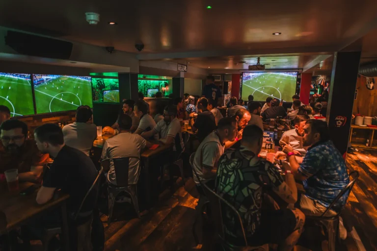 Crowded sports bar with fans watching soccer on multiple large screens.
